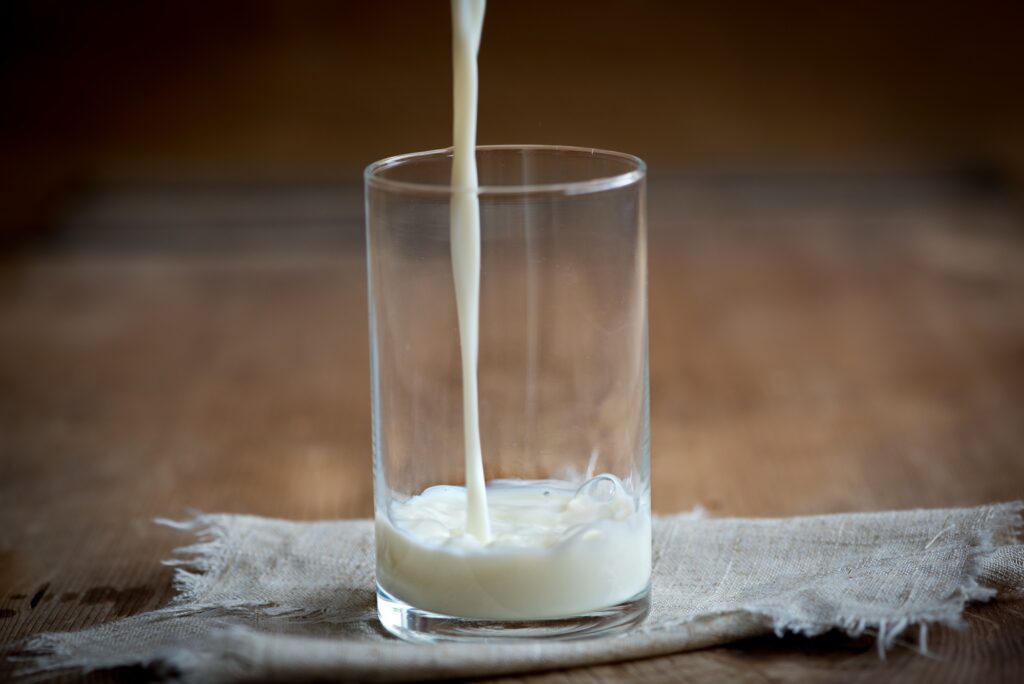Milk being poured into a glass sitting on a table.