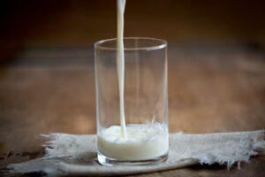 Milk being poured into a glass sitting on a table.
